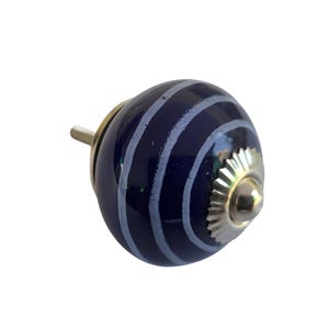 May include: A navy blue ceramic cabinet knob with a silver metal base and a silver metal stem. The knob has a striped pattern in light blue. The knob is round and has a decorative design.