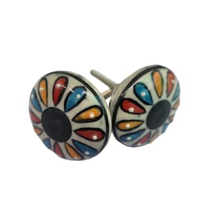 May include: Two decorative ceramic cabinet knobs. Each knob features a white base with a black center and colorful petal-like designs in red, blue, orange, and yellow. The knobs have a silver-colored stem.