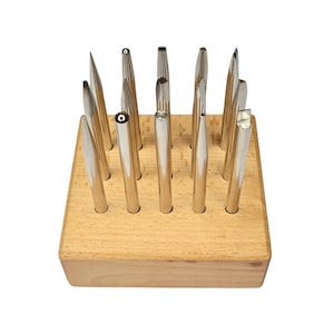 May include: A collection of silver metal tools with various shaped tips, displayed in a light brown wooden block. The tools are arranged vertically, showcasing their different designs. The block has multiple holes to hold the tools.