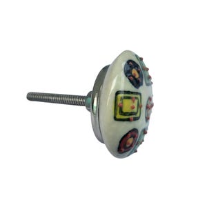 Peut inclure: Un bouton de meuble d&eacute;coratif avec une face en c&eacute;ramique ovale de couleur cr&egrave;me. La face est orn&eacute;e de formes g&eacute;om&eacute;triques color&eacute;es, notamment des carr&eacute;s, des cercles et des points jaunes, rouges et noirs. Le bouton a une base en m&eacute;tal argent&eacute; et une vis filet&eacute;e pour la fixation.