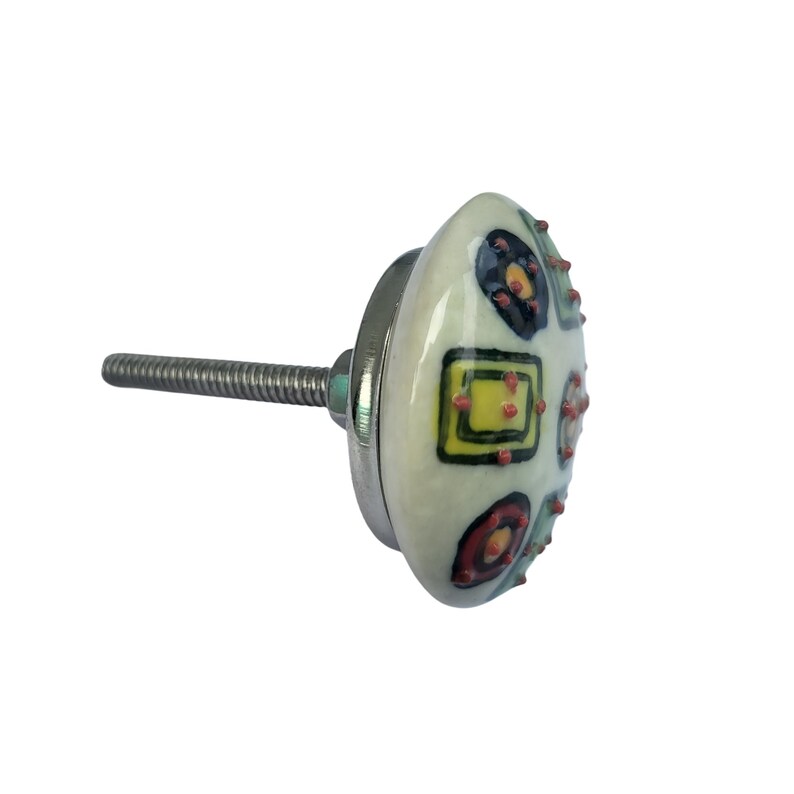 Peut inclure: Un bouton de meuble d&eacute;coratif avec une face en c&eacute;ramique ovale de couleur cr&egrave;me. La face est orn&eacute;e de formes g&eacute;om&eacute;triques color&eacute;es, notamment des carr&eacute;s, des cercles et des points jaunes, rouges et noirs. Le bouton a une base en m&eacute;tal argent&eacute; et une vis filet&eacute;e pour la fixation.