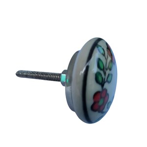 May include: A ceramic cabinet knob with a floral design. The knob is off-white with a red and green floral pattern. It has a metal screw for installation.