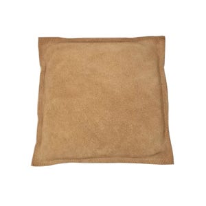 May include: A tan suede pillow with a square shape and a subtle texture.