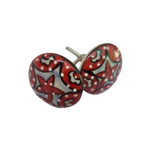 May include: Two ceramic cabinet knobs with a floral design. The knobs are oval-shaped with a red background, white polka dots, and a red star-shaped flower design. The hardware is silver.