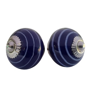 May include: Two navy blue ceramic cabinet knobs with a striped design in light blue. Each knob has a silver-coloured metal base and a small, round silver-coloured centre. The knobs are for furniture or home decor.