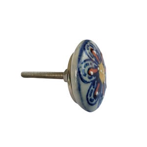 May include: A decorative ceramic cabinet knob with a floral design. The knob features a white base with a blue floral pattern, accented with orange and yellow details. It has a metal screw for installation.
