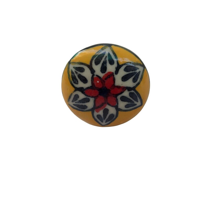 Op de afbeelding: Ronde, gele keramische kastknop met een bloemmotief. De bloem heeft een rood hart, witte bloemblaadjes en donkergroene bladaccenten. De knop is een decoratief hardware-element.