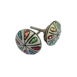 May include: Two decorative ceramic cabinet knobs. Each knob has a white background with a colorful, stylized floral design in red, blue, green, and orange. The knobs are mounted on silver-colored screws.