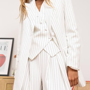 May include: White pinstripe blazer, vest, and wide-leg pants. The suit features a double-breasted blazer with notched lapels, a matching vest, and high-waisted pants. The pinstripes are a dark gray color.