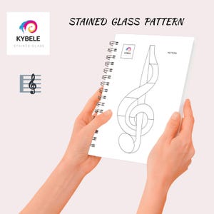 May include: A white spiral-bound notebook held by hands, featuring a stained glass pattern of a treble clef. The notebook has the text "STAINED GLASS PATTERN" at the top. The Kybele logo is in the upper left corner.