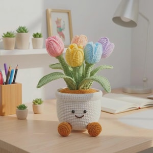 May include: A crochet tulip bouquet in a white, round, textured pot with a smiling face and two small brown feet. The flowers are in shades of pink, yellow, light blue, and lavender, featuring green stems and leaves. The pot has a brown top.