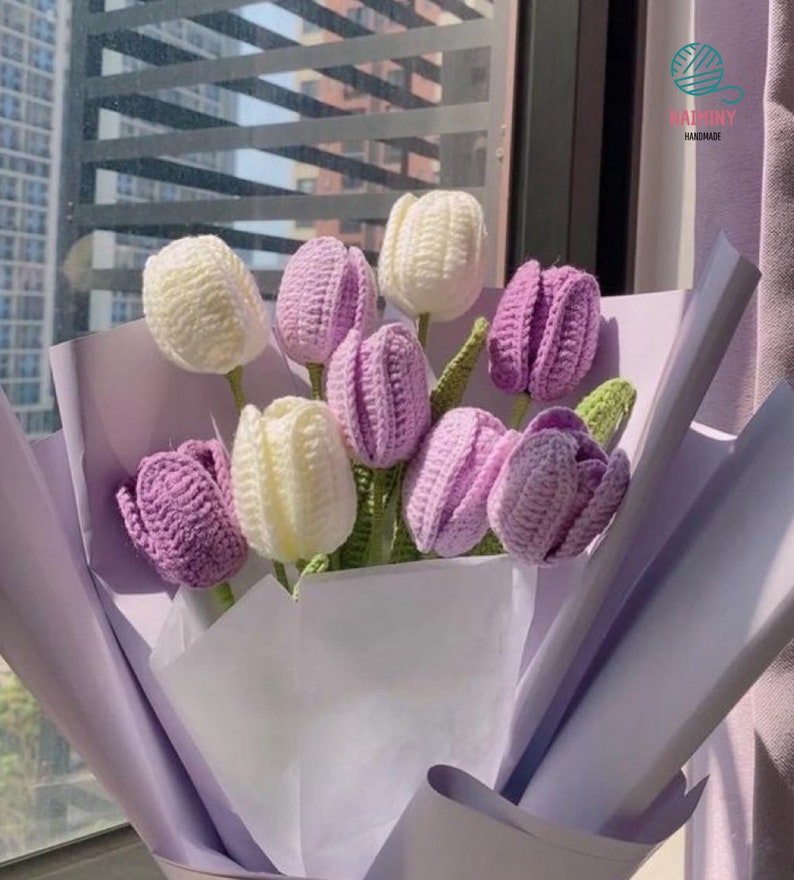 May include: A bouquet of crocheted purple and white tulips wrapped in light purple tissue paper. The bouquet is labeled "Raiminy Handmade".