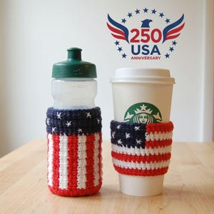 May include: A clear water bottle and a white coffee cup, both adorned with crocheted cozies. The cozies feature a design inspired by the American flag, with red and white stripes and a blue field with white stars. The image also includes a graphic that says "250 USA Anniversary".