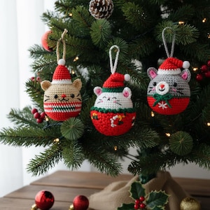 May include: Three handmade crochet cat ornaments hanging on a Christmas tree. Each ornament features a cat face wearing a Santa hat. The ornaments are red, white, beige, and gray, with details like whiskers and a festive bow.