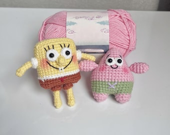 May include: Crocheted SpongeBob SquarePants and Patrick Star figures in yellow, brown, pink, and green. A pink yarn ball is in the background. The figures have black eyes and smiling faces. The figures are handmade.