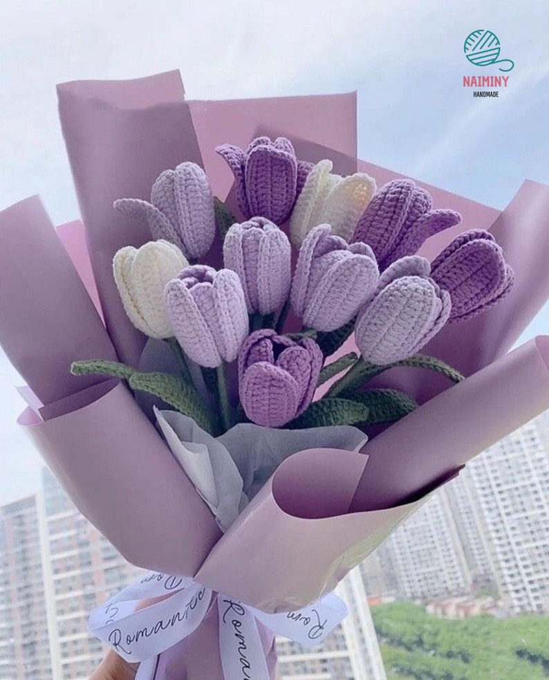May include: A bouquet of crocheted purple and white tulips wrapped in lavender paper with a white ribbon that says "Romantic" in cursive.