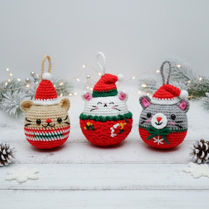 May include: Three crocheted Christmas ornaments shaped like cats and mice. Each ornament has a red and white Santa hat. The cat ornaments are tan, white, and gray, with red and green accents. Each has a loop for hanging.