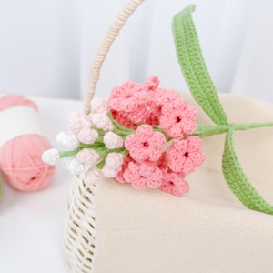 Puede incluir: Un ramo de flores de ganchillo rosa y blanco con tallos verdes en una cesta de mimbre blanca.