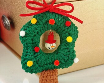 May include: A handmade green crochet Christmas tree ornament with a red bow and a snowman in the center. The tree is decorated with colorful pom-poms and has a brown trunk. The text "keep happy" is written in white cursive.