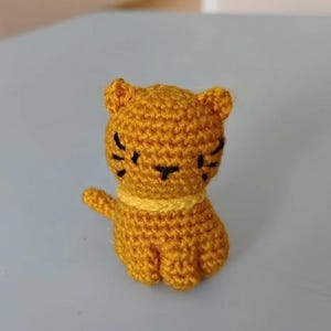 May include: A small crocheted cat toy in a yellow colour. The cat has black embroidered eyes and a black nose.