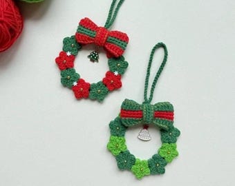 May include: Two handmade crochet Christmas wreath ornaments. Each wreath is green with red and white accents, a red and green bow, and a small tree charm. The wreaths are hanging by green loops.