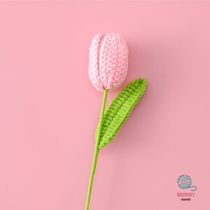 May include: A pink crocheted tulip with a green crocheted leaf and stem. The flower is on a pink background.