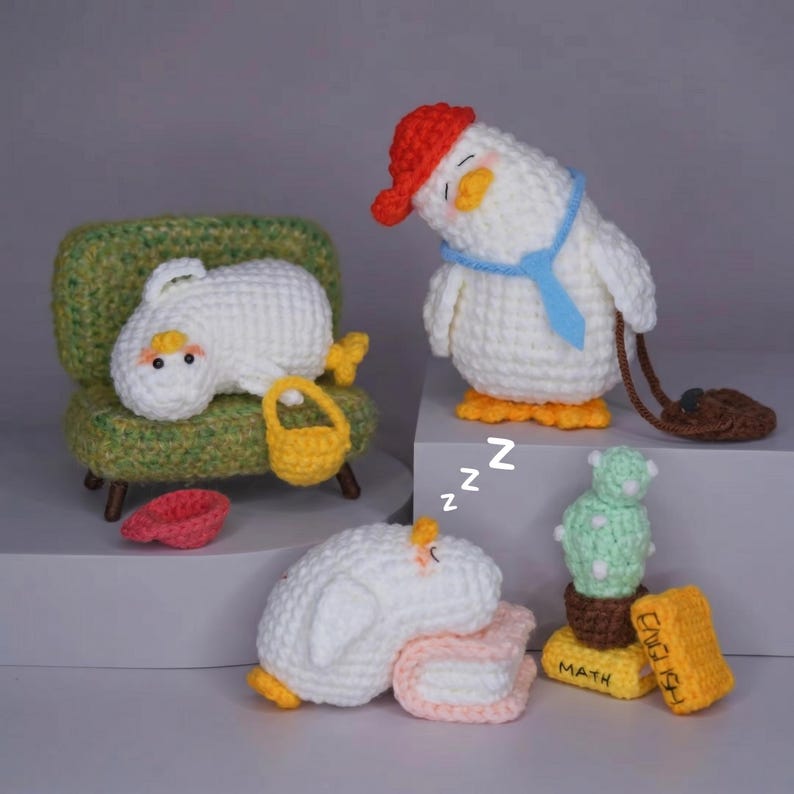 May include: Three white crocheted duck figures with orange beaks and feet. One sits on a green textured couch with a yellow basket, one stands wearing a red cap and blue tie with a brown bag, and one sleeps on a pink book near a cactus and books labeled MATH and ENGLISH.