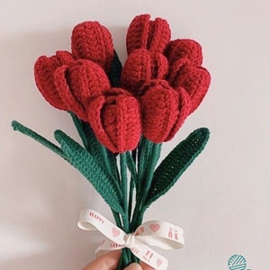 May include: A bouquet of crocheted red tulips with green leaves tied together with a white ribbon that says "Happy" and "Love" in red lettering.