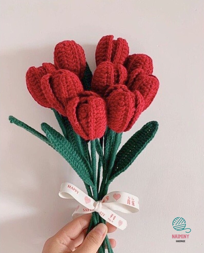 May include: A bouquet of crocheted red tulips with green leaves tied together with a white ribbon that says "Happy" and "Love" in red lettering.