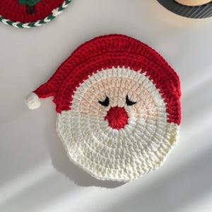 Peut inclure: Un dessous de verre fait main en crochet représentant le Père Noël. Il arbore un bonnet rouge, une barbe blanche et un visage rose avec des yeux fermés et un nez rouge. Un article décoratif et festif pour les fêtes de fin d'année.