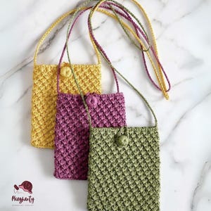 May include: Three handmade crochet phone bags in yellow, purple, and green, each with a matching button closure and long strap. The bags have a textured, diamond-like pattern. The background is a white marble surface.