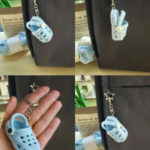 Op de afbeelding: Een lichtblauwe gehaakte klomp-sleutelhanger met een kleine witte knoop aan de zijkant en een zilverkleurige stervormige sluiting aan een metalen ketting. Het miniatuur schoeisel heeft een textuur met geperforeerde gaatjes.