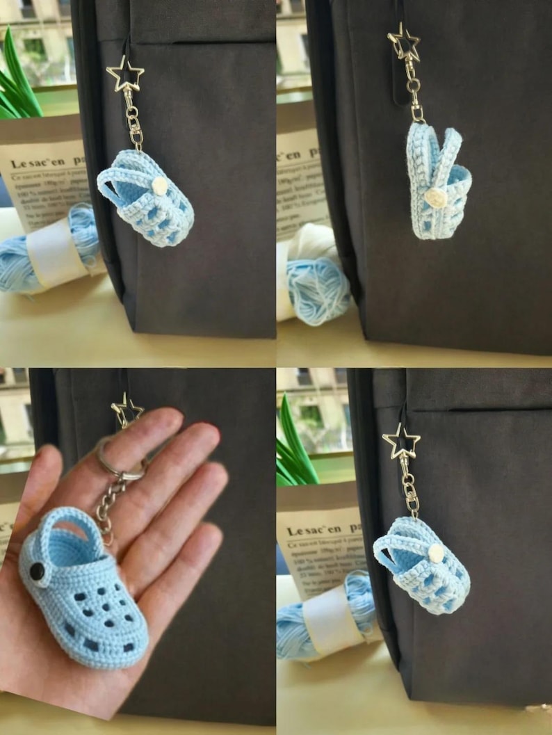 Op de afbeelding: Een lichtblauwe gehaakte klomp-sleutelhanger met een kleine witte knoop aan de zijkant en een zilverkleurige stervormige sluiting aan een metalen ketting. Het miniatuur schoeisel heeft een textuur met geperforeerde gaatjes.
