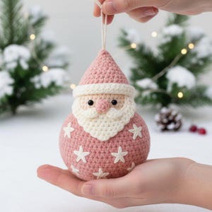 以下が含まれることがあります： 手作りのピンク色のサンタクロースのクリスマスオーナメント。白いひげ、帽子のトリム、星のアクセントが特徴です。サンタクロースは黒い目と小さなピンクの鼻をしています。吊り下げ用の白い紐が付いています。