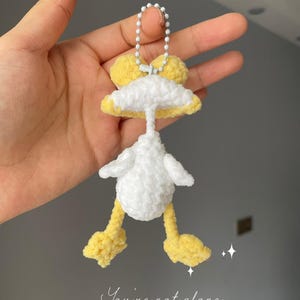 May include: A handmade crochet duck keyring in white and yellow. The duck has a white body, yellow feet and head, and a small white bow. The text "You're not alone" is written in cursive at the bottom.