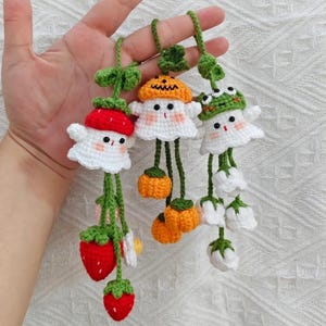 Puede incluir: Tres adornos de ganchillo hechos a mano con forma de personajes caprichosos. Uno es una fresa, otro una calabaza y el tercero una rana. Cada uno tiene un cuerpo blanco y detalles verdes. Los adornos están suspendidos por hilo verde.