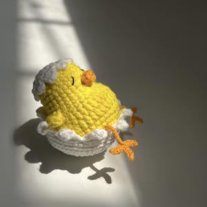Può includere: Un pulcino all'uncinetto che esce da un uovo bianco. Il pulcino è giallo con becco e zampe arancioni. Il guscio dell'uovo ha un bordo smerlato. Questo articolo a tema pasquale è ideale per le decorazioni primaverili.