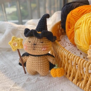 Può includere: Un coniglietto di Halloween all'uncinetto con un cappello da strega nero e un mantello, che tiene in mano una bacchetta a stella e una piccola zucca arancione. Il coniglietto è marrone chiaro con guance rosa. Filato nero, arancione e giallo in un cestino di vimini.