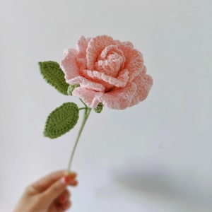 May include: A crocheted pink rose with green leaves and a stem.