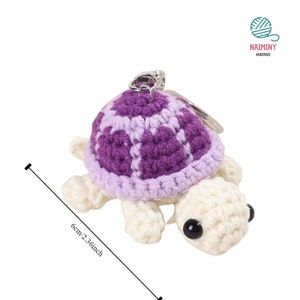 Op de afbeelding: Een gehaakte schildpad sleutelhanger met een paarse en witte schil. De schildpad is ongeveer 6 cm of 2,36 inch hoog.