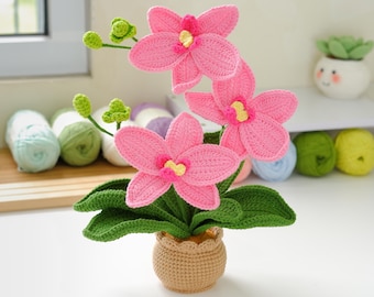 Puede incluir: Una planta de orquídea hecha a mano con ganchillo, con flores rosas brillantes, hojas verdes y una maceta beige. Las flores tienen centros amarillos. Esta planta decorativa es ideal para añadir un toque de encanto artesanal.