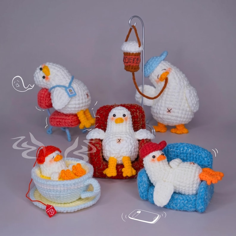 May include: Five crocheted white duck figures with orange beaks and feet. One sits in a red chair, one in a blue chair, one in a tea cup, one leans on a red chair, and one stands with a coffee cup hanging from a metal stand. Includes line art.