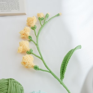 May include: A crocheted flower bouquet with yellow flowers and green leaves. The flowers are in the shape of bells and the leaves are long and narrow.