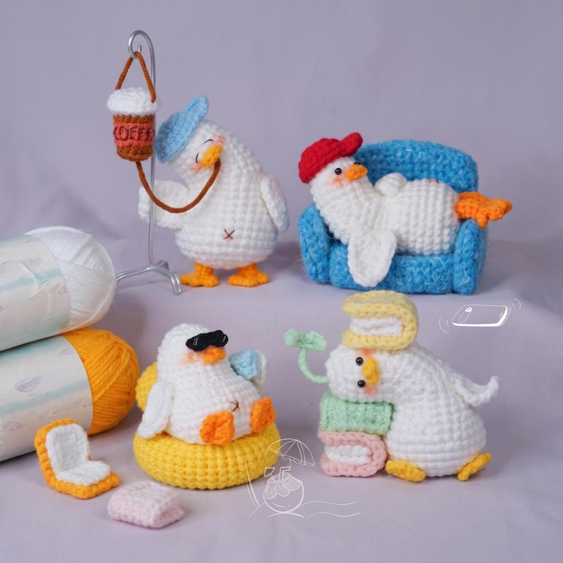 May include: Four white crocheted duck figures with orange feet. One wears a blue cap and holds a coffee cup, one rests on a blue sofa wearing a red cap, one wears black sunglasses in a yellow float, and one sits with stacked books and a green sprout.
