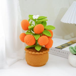 May include: A handmade crochet orange tree featuring vibrant orange fruit, green leaves, and a small white flower. The tree is potted in a brown crochet pot. This decorative tree is a unique home decor item.