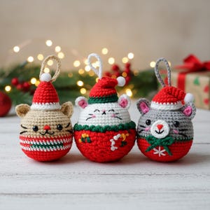 May include: Three handmade crochet Christmas ornaments shaped like mice. Each mouse wears a red Santa hat with a white pom-pom. The mice have different colors: tan, white, and gray. The ornaments have a loop for hanging and are decorated with red, green, and white details.
