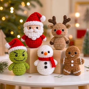May include: A set of five crocheted Christmas ornaments including a Santa Claus, a reindeer with a red nose, a green character in a Santa hat, a snowman with a red scarf, and a gingerbread person, all arranged on wooden blocks.