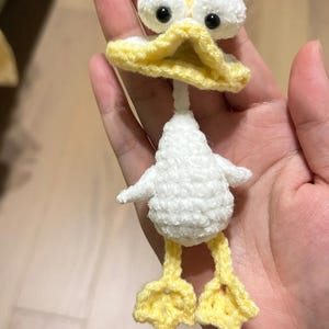 May include: A crocheted duck toy, featuring a white body, yellow beak, and feet. The duck has large white eyes with black pupils. The duck's body is fluffy white, and the beak and feet are bright yellow. A charming, handcrafted item.