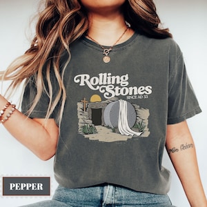 May include: A gray t-shirt with a vintage-style graphic of a stone tomb with a white sheet draped over it. The text "Rolling Stones Since AD 33" is above the tomb.