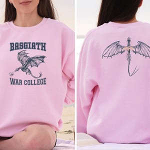 May include: Pink sweatshirt with a dragon graphic and the text "Basgiath War College" on the front. The back of the sweatshirt features a dragon graphic.